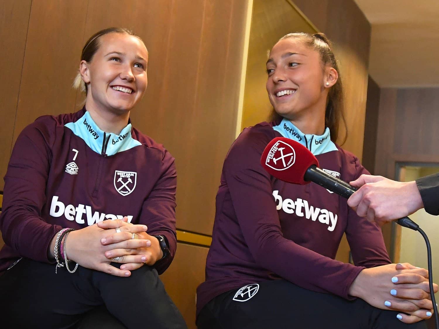 A woman and a girl in West Ham football jerseys being interviewed at a press conference.