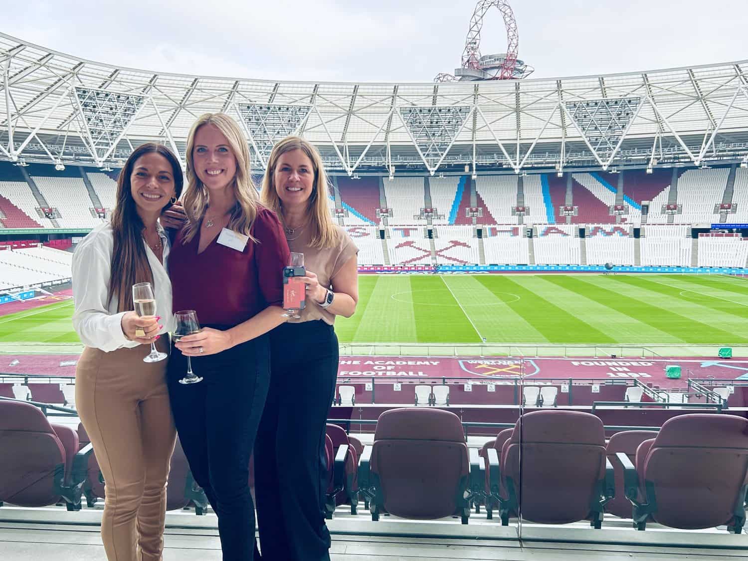 Celebration at the stadium with three women holding drinks, smiling and enjoying the event.