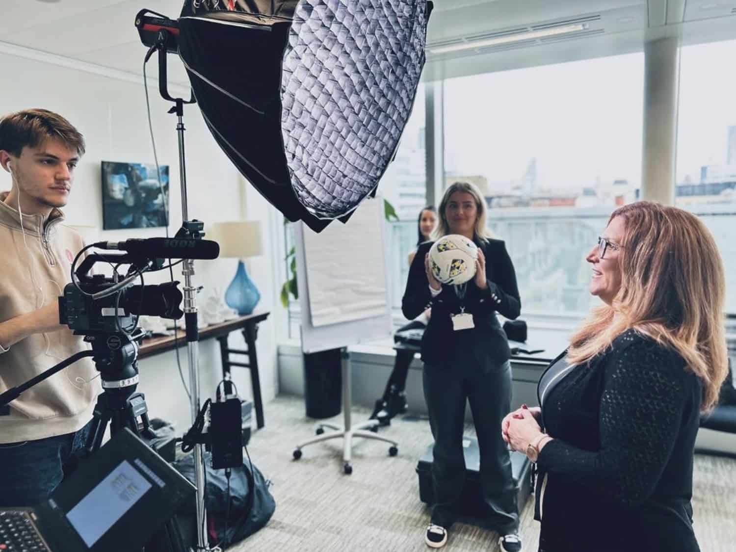 Professional video shoot in modern office with woman presenter and crew, corporate filming setup.