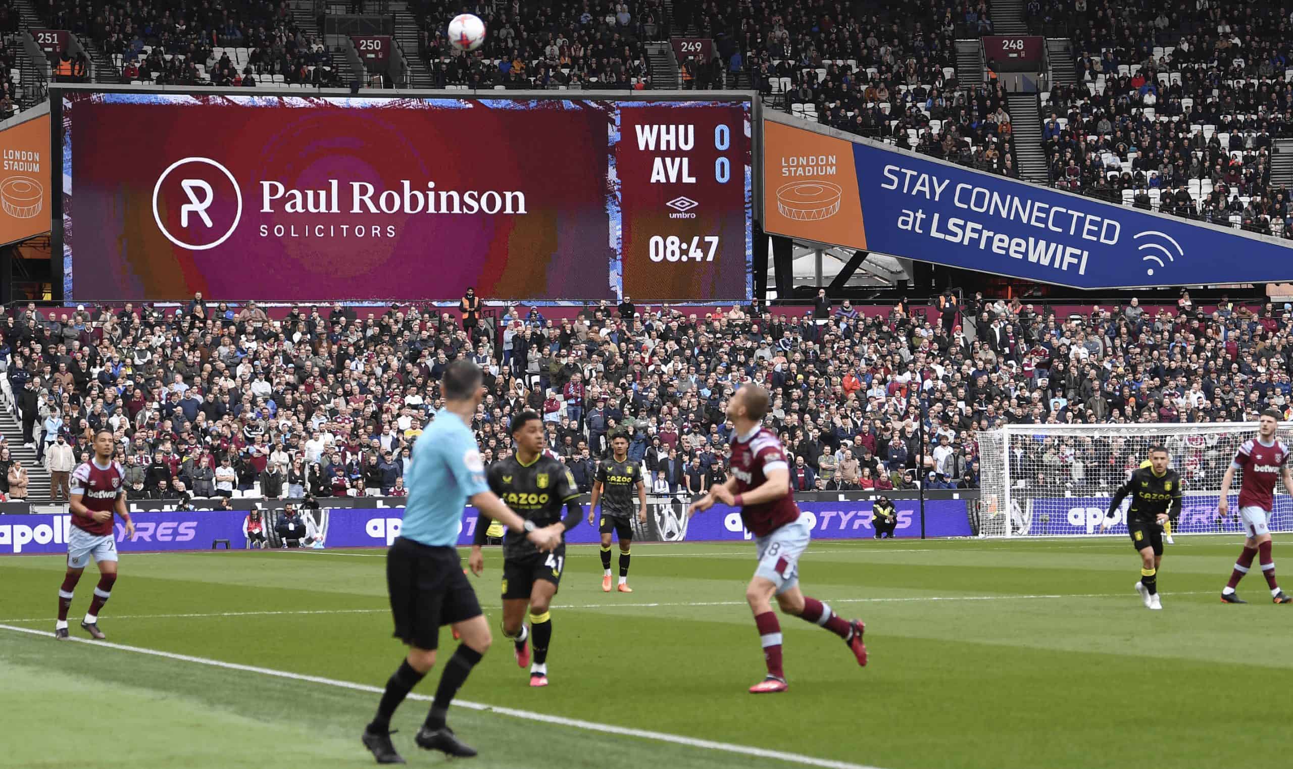 A football match at a stadium with players in action and a large crowd in the background.
