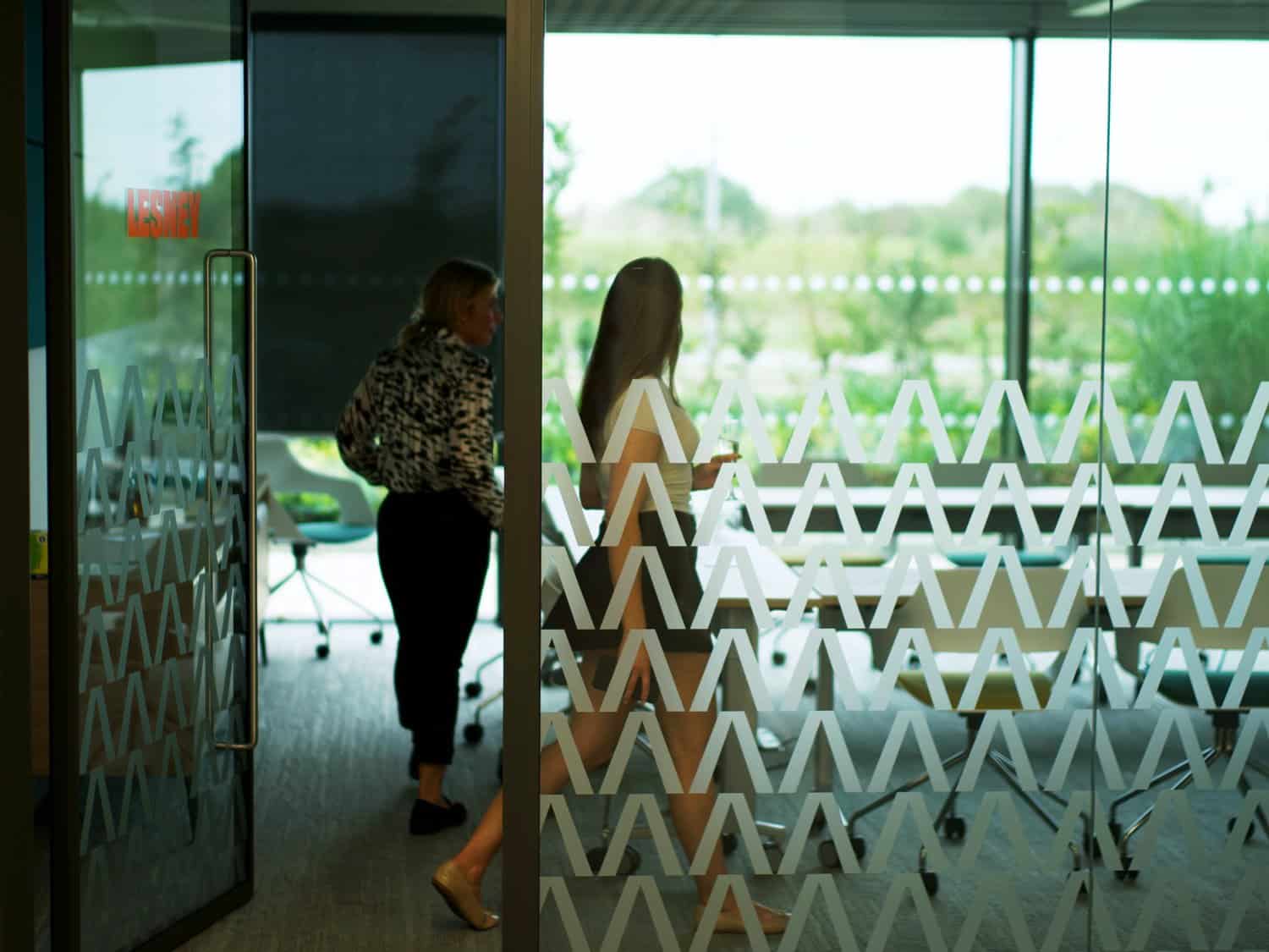 A woman and a girl talking inside a modern office with glass walls and patterned decals.