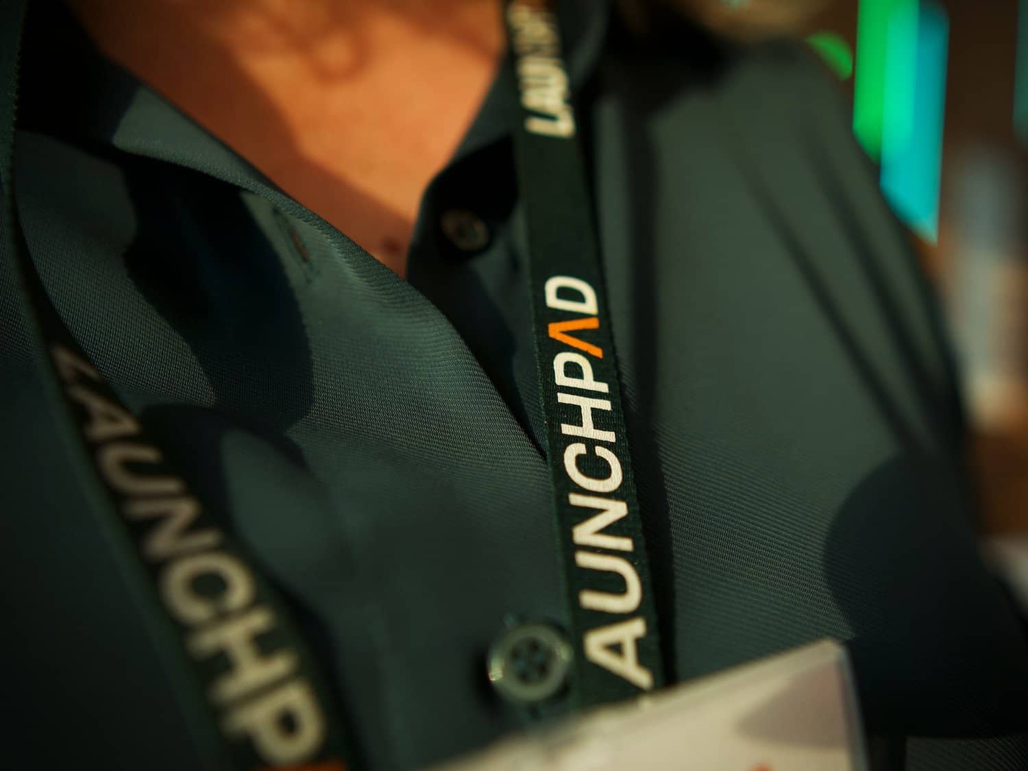 A professional person wearing a dark green polo shirt with a lanyard reading