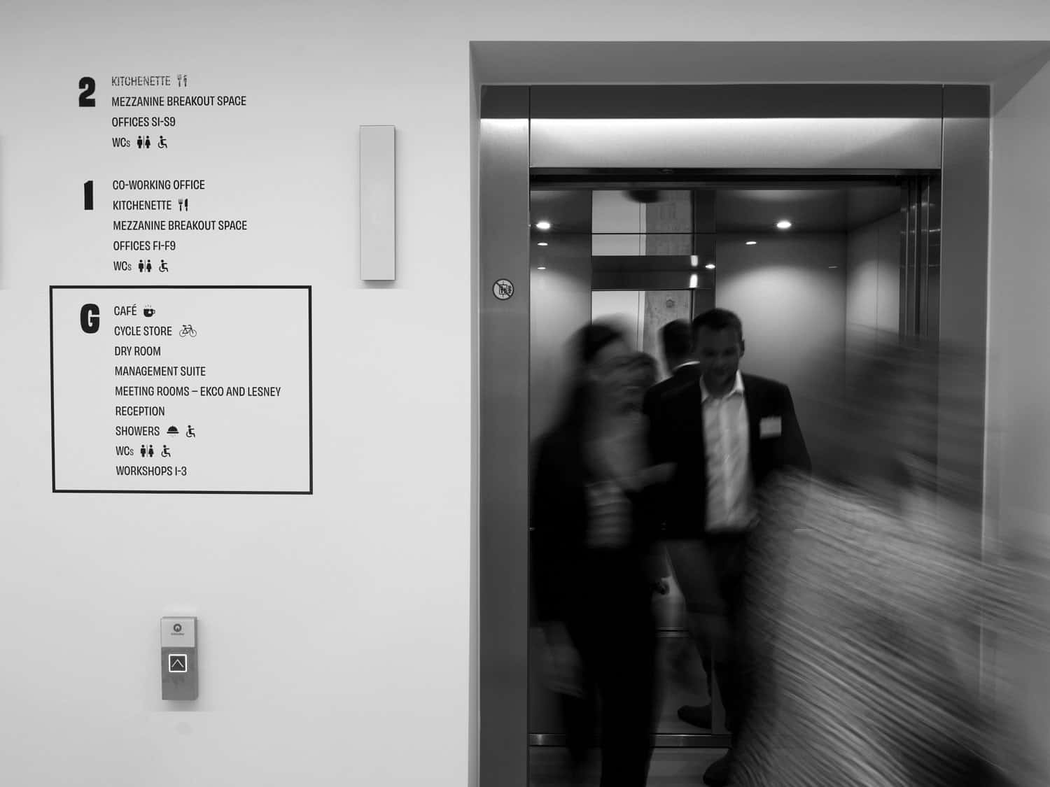 Modern office elevator with people entering, corporate workspace environment, black and white image.