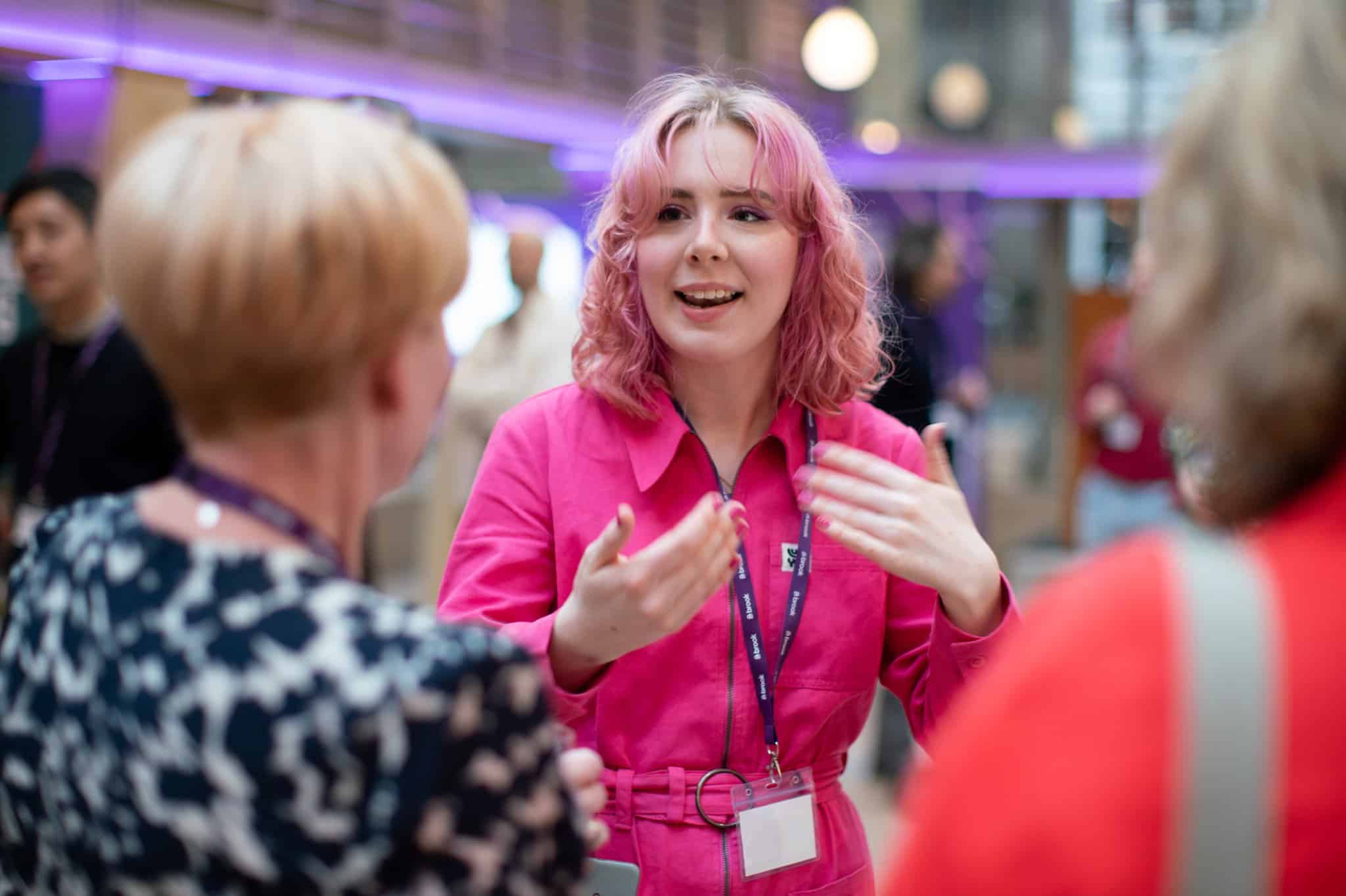 A woman in a pink uniform engaging in conversation at a professional event or conference.