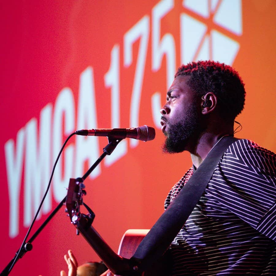 A vibrant musician performing live on stage with a guitar at a music event.