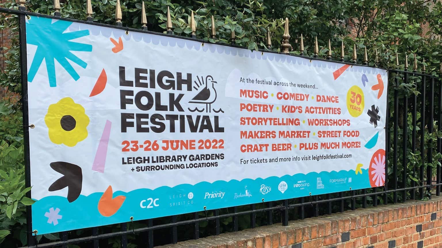 A vibrant banner advertising the Leigh Folk Festival 2022, featuring music, comedy, dance, and famil.