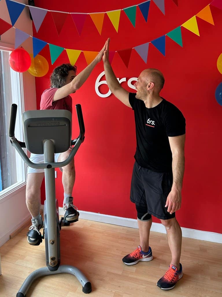 High-five between trainer and client during fitness session at 6rs gym with colourful decorations.