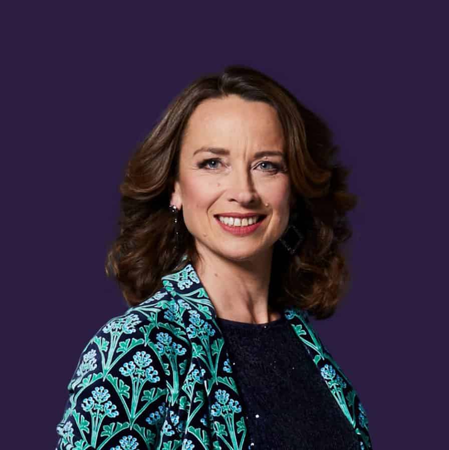 Elegant woman with brown hair wearing a patterned blue and black blazer, smiling confidently.