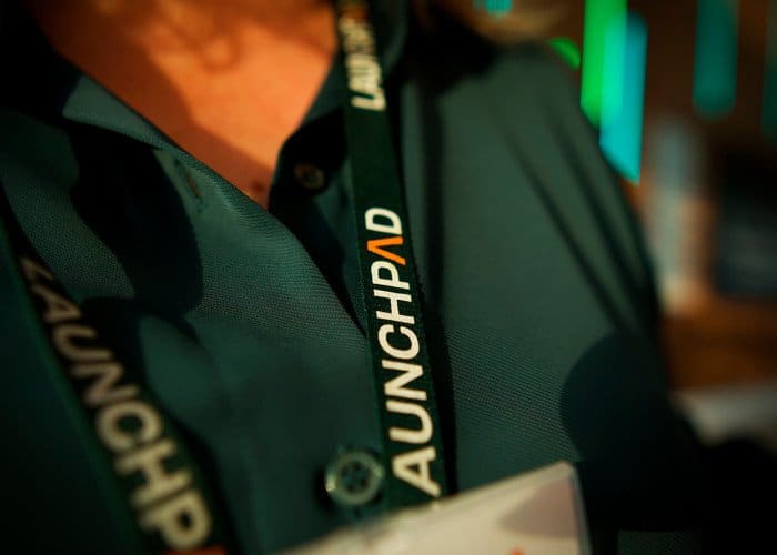 A professional person wearing a dark green polo shirt with a lanyard at a conference or event.