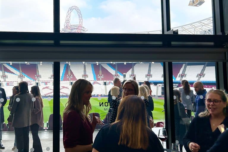 A vibrant group of people socialising inside a modern stadium with a view of the amusement park outs.