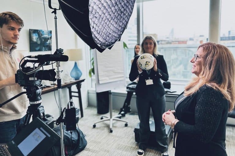 A professional woman being filmed in a modern office studio with lighting equipment.
