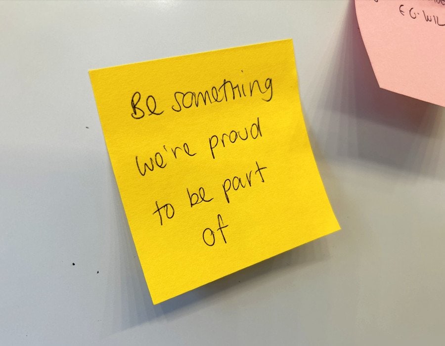 Be someone we're proud to be part of - motivational sticky note on whiteboard.