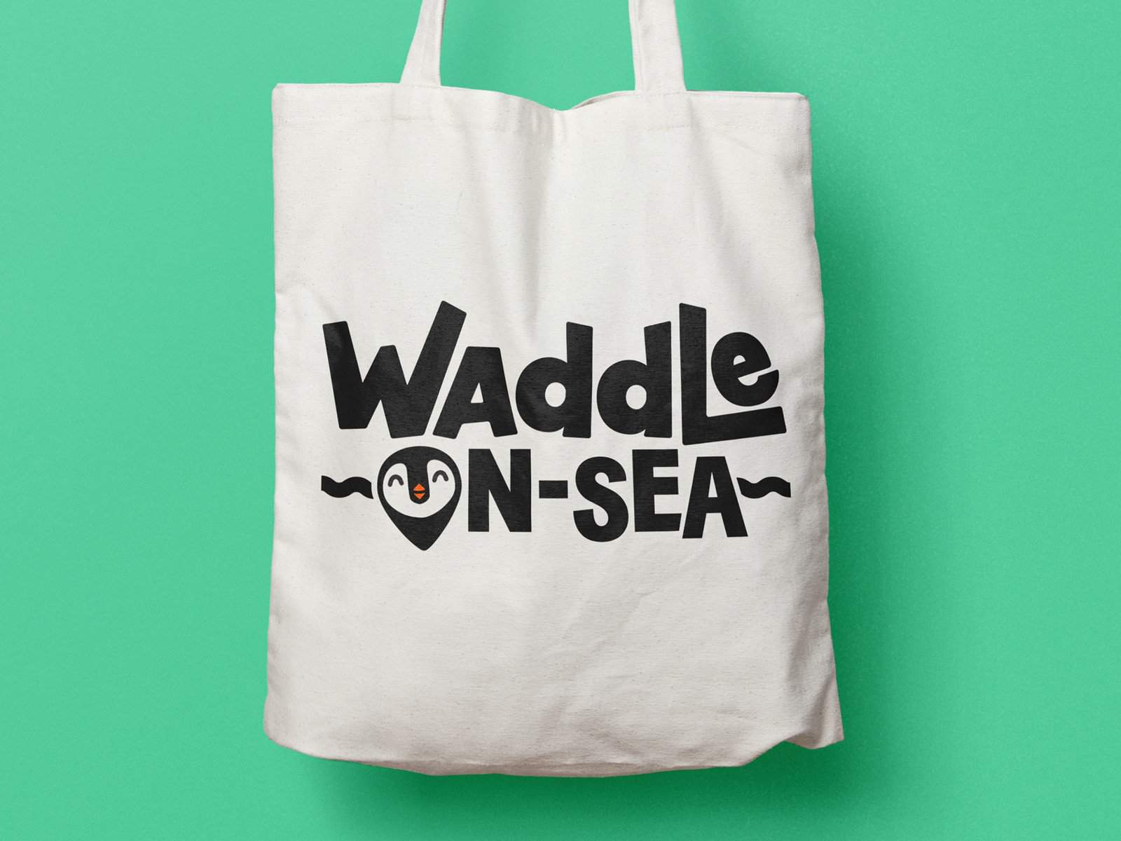 Waddle On-Sea tote bag with playful penguin logo on white fabric against green background.