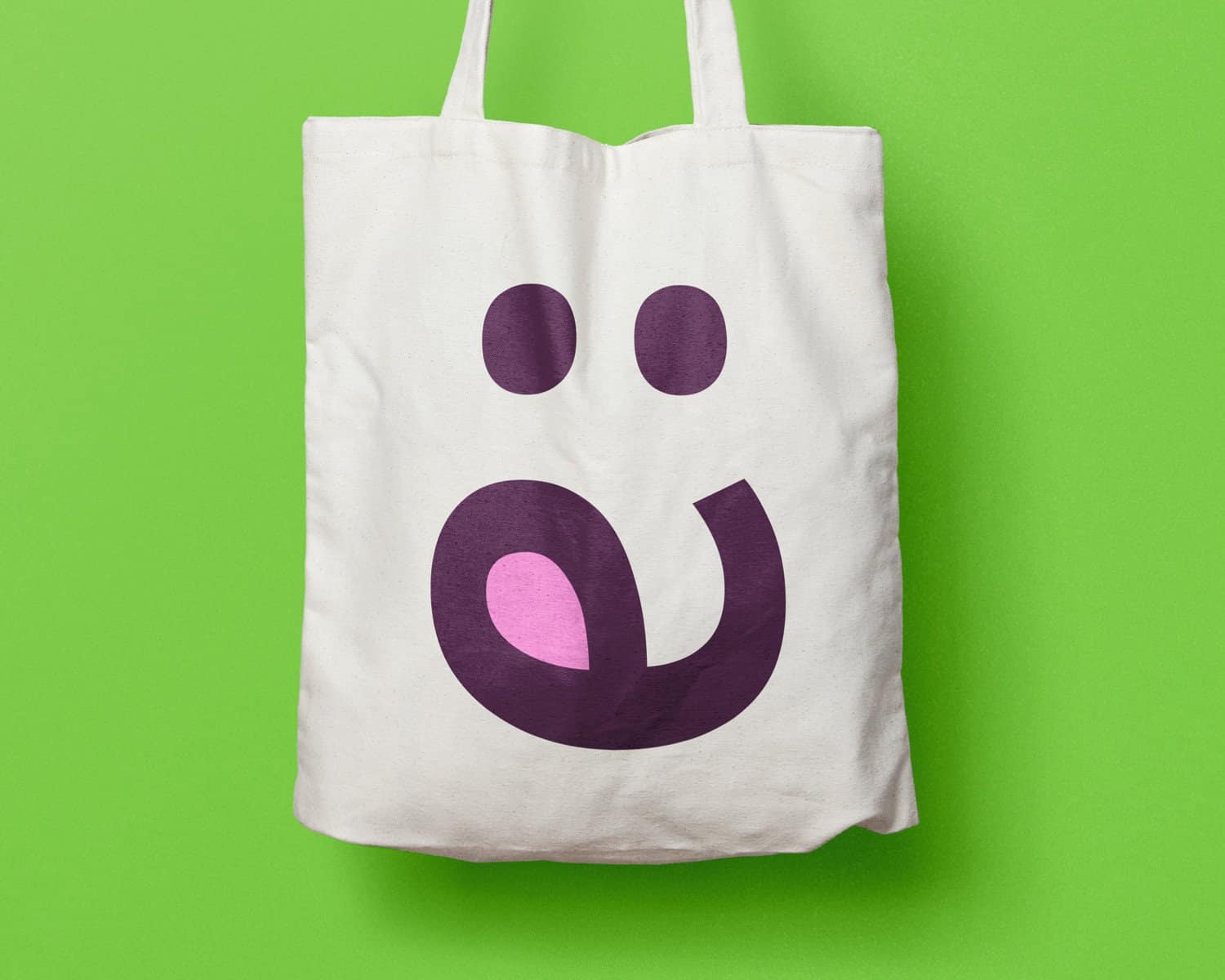 A tote bag with a playful purple smiley face design on a green background.