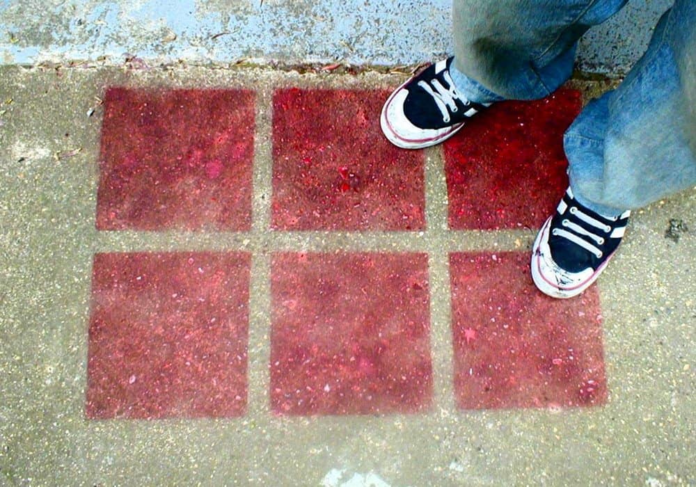 A colourful hopscotch game painted on the pavement with a person wearing sneakers standing nearby.
