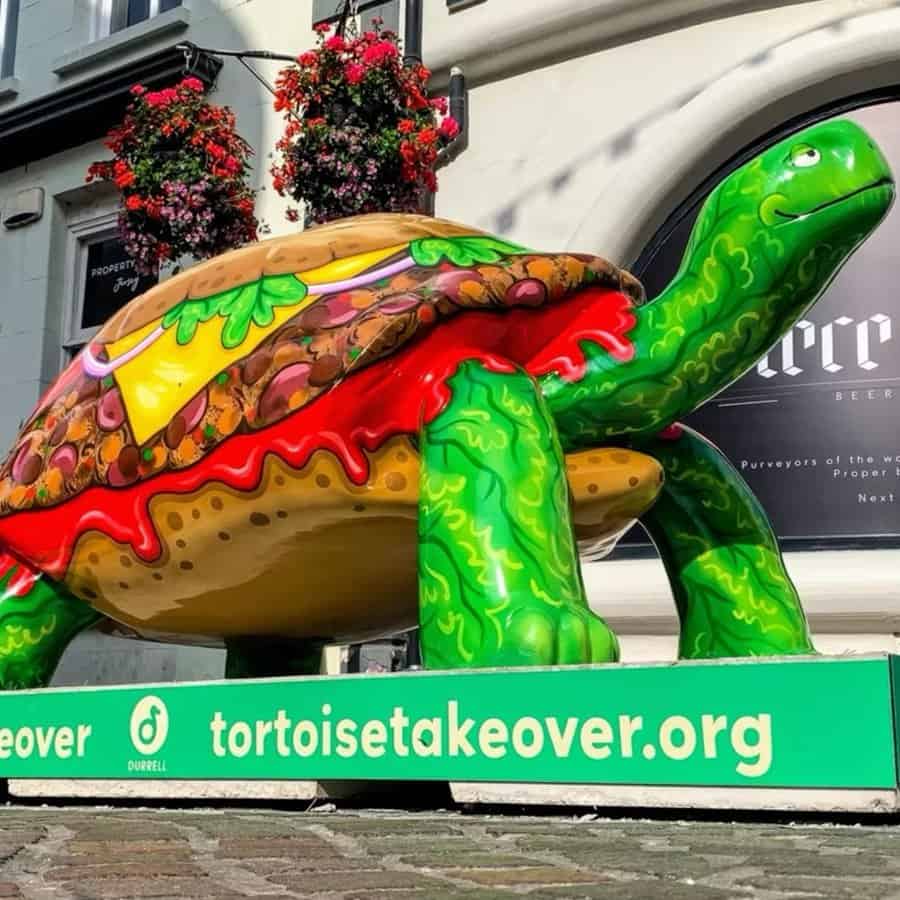 A colourful turtle sculpture with a burger shell, displayed outdoors on a city street.