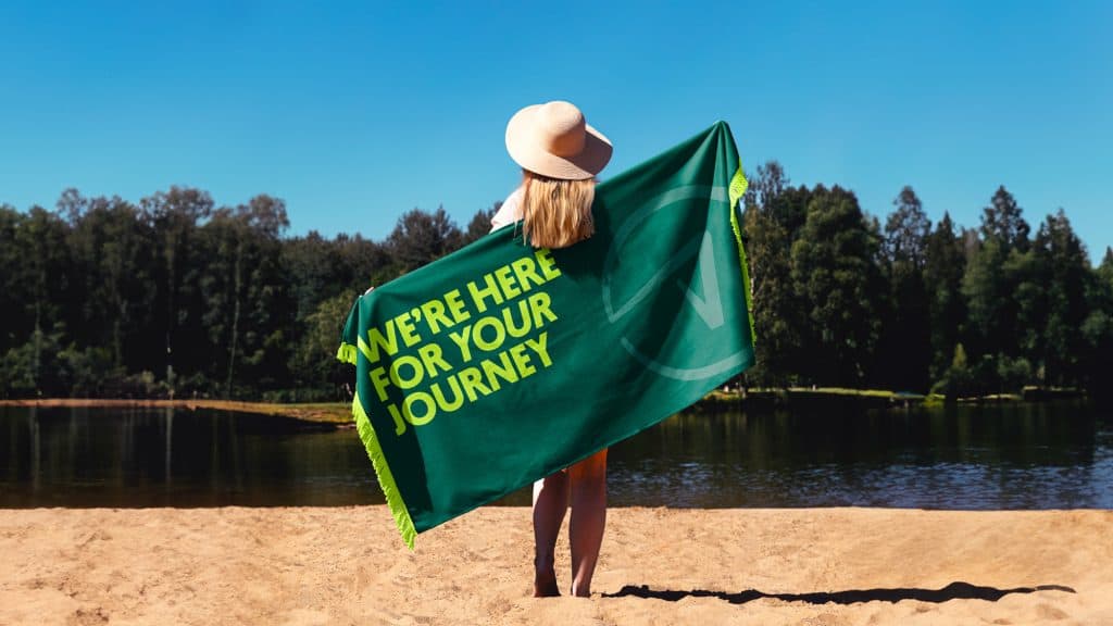 Relaxed woman with a green towel at the beach, scenic lake and trees in background.