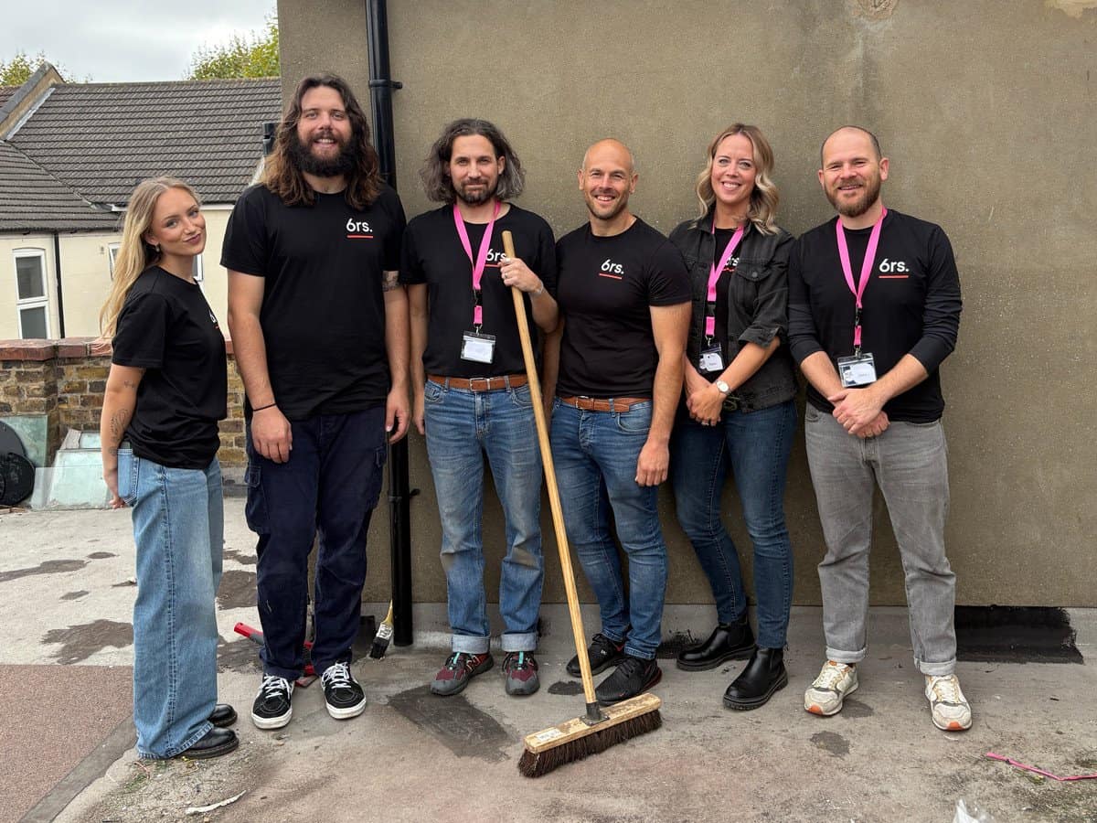Clean and modern team of six people wearing branded black t-shirts, standing outdoors.