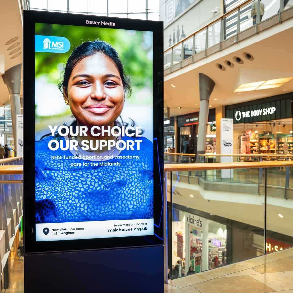 NHS-funded abortion and vasectomy support digital billboard in shopping mall.
