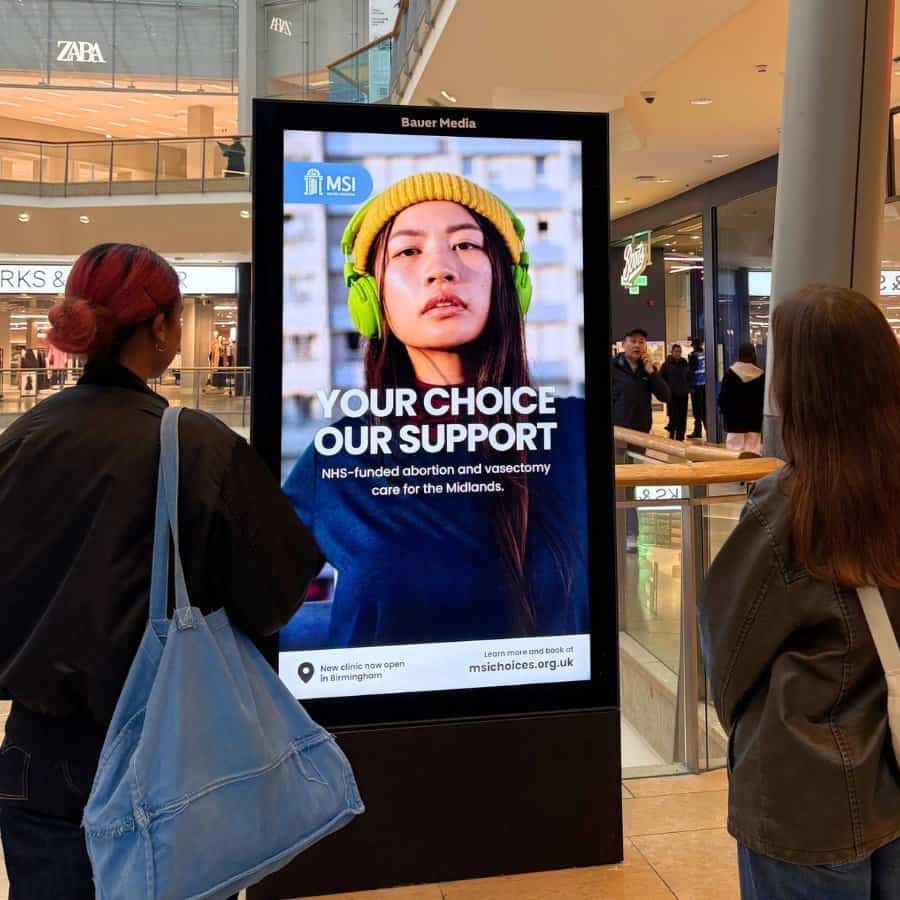 NHS abortion and vasectomy support digital billboard in shopping mall, UK.