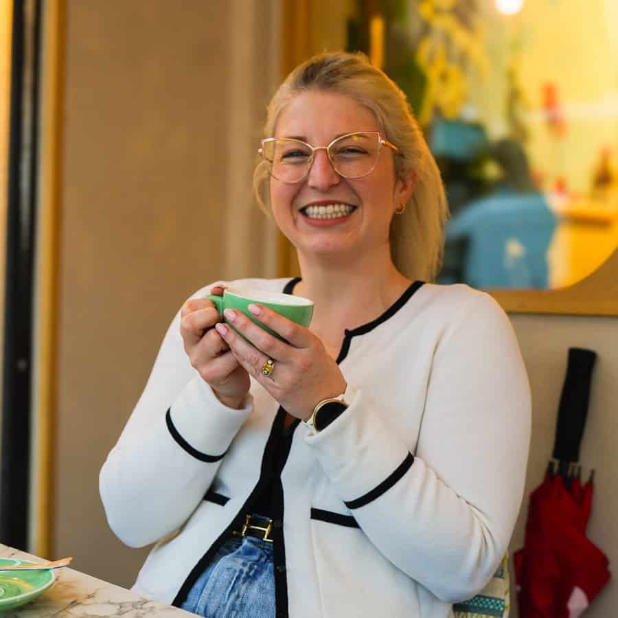 A smiling woman enjoying a hot drink in a cozy cafe setting.
